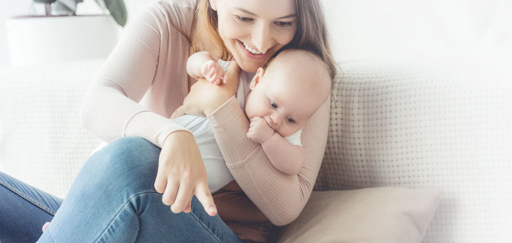A woman holding her baby while using her laptop