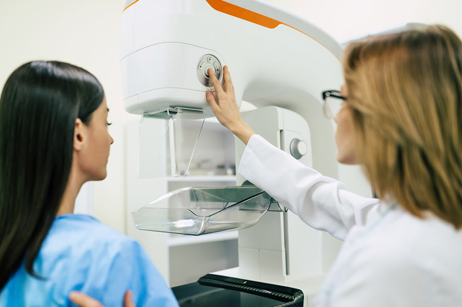 Female patient standing next to a mammogram machine with a female doctor